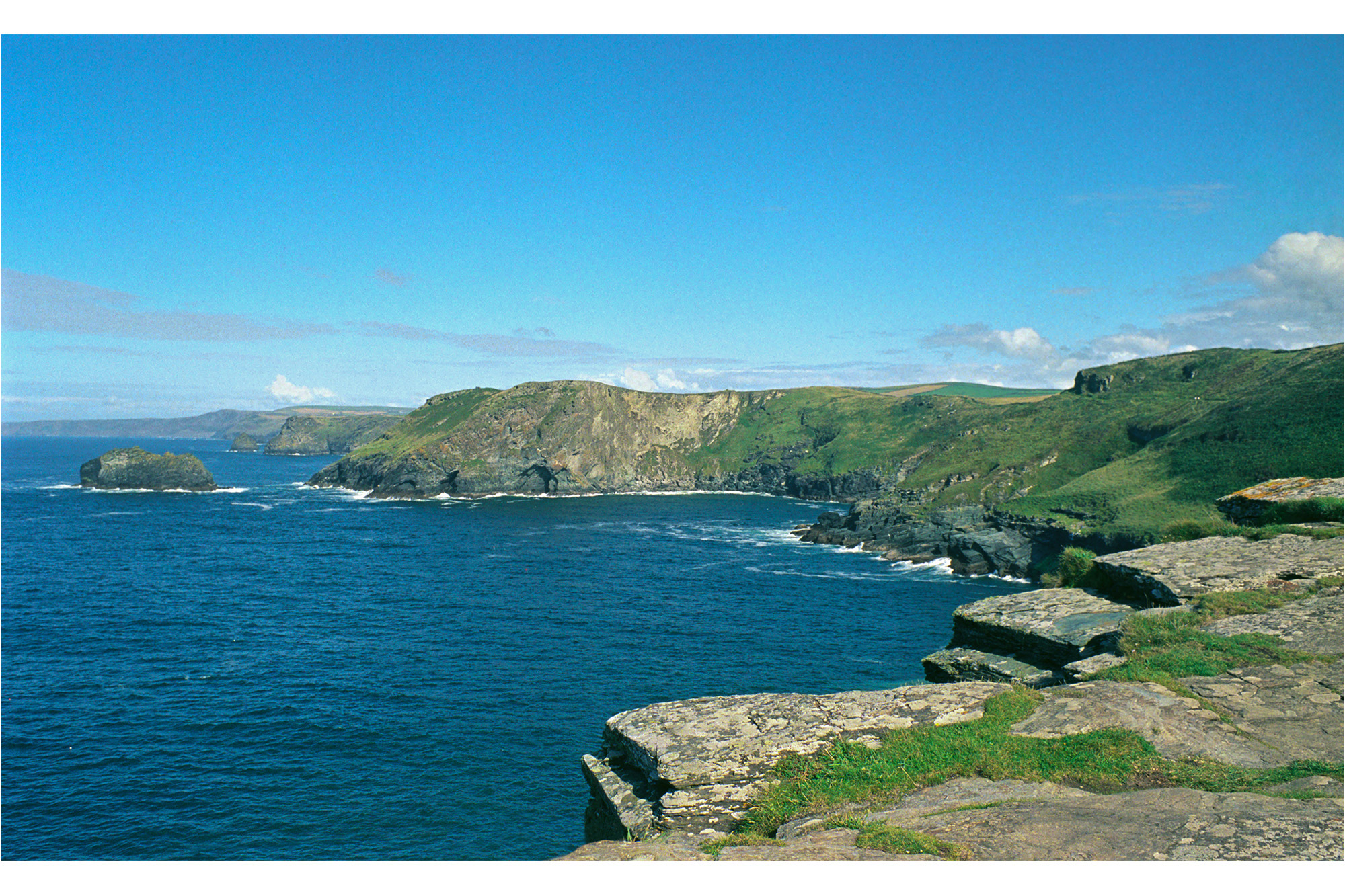An elevated scene of the Cornish coastline, flat rock formation juts out above the sea.
