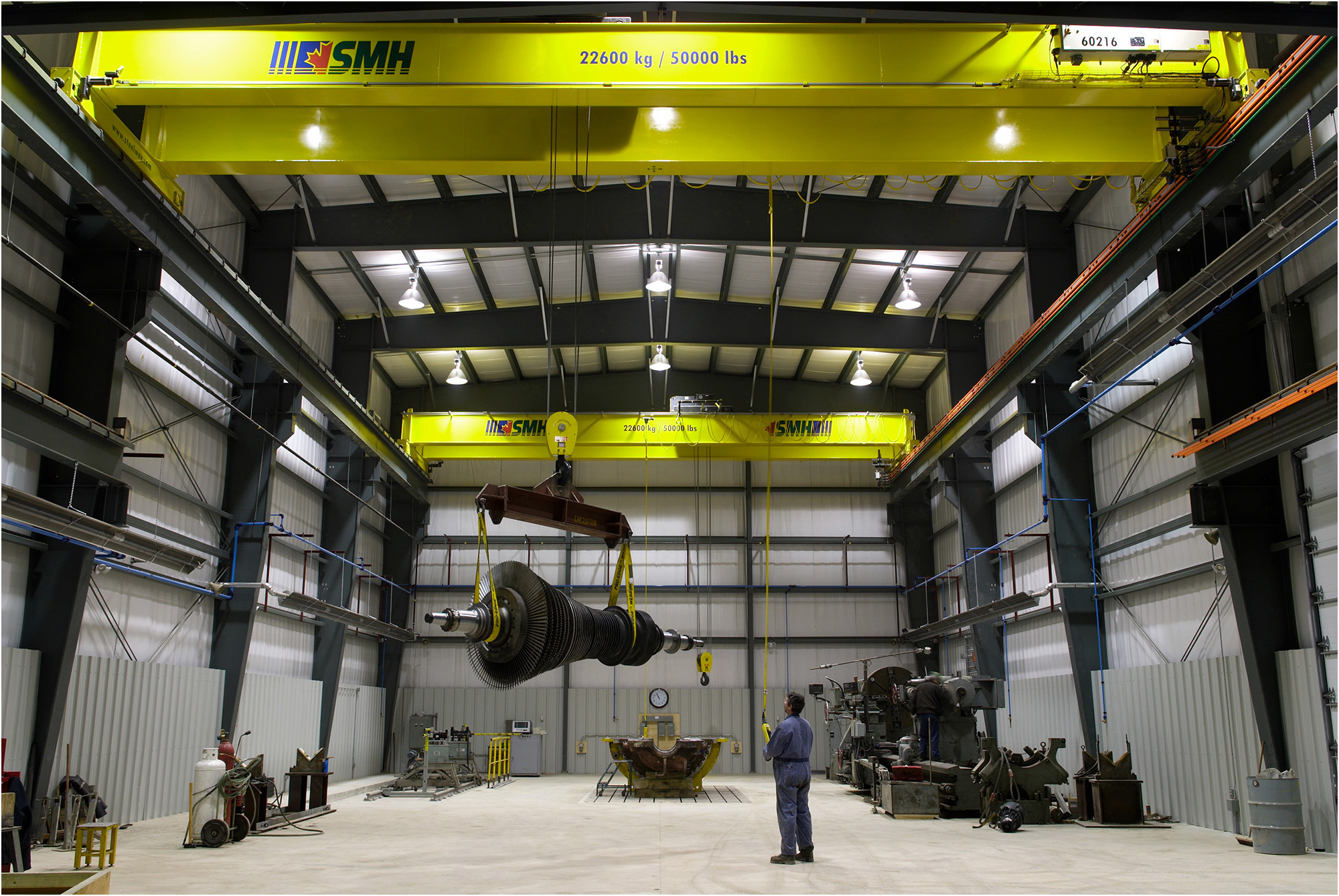 A man operates a hoist to lift a very large turbine.